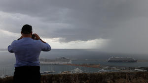 23.10.2019, Spanien, Palma de Mallorca: Ein Tourist fotografiert dunkle Regenwolken über der Bucht und dem Hafen, in dem zwei Kreuzfahrtschiffe liegen. Rund ums Mittelmeer haben heftige Unwetter vielerorts Überflutungen und Schäden  verursacht. Foto: Clara Margais/dpa +++ dpa-Bildfunk +++