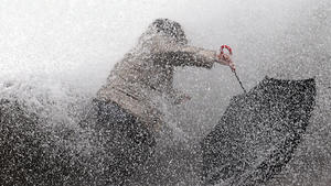 dpatopbilder - 22.12.2019, Frankreich, Biarritz: Eine Frau versucht mit ihrem Regenschirm gegen eine Welle anzukämpfen, die den Hafendamm vor der Atlantikküste erreicht.  In Südwestfrankreich hat der Wintersturm "Fabien" Geschwindigkeiten von bis zu 150 Stundenkilometern erreicht. Foto: Bob Edme/AP/dpa +++ dpa-Bildfunk +++