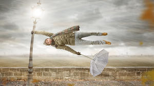 A funny man with an umbrella is holding on to a lamp post while a heavy storm ist blowing. The man is flying horizontally in mid air.