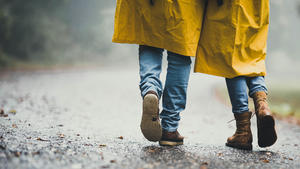 Rear view of unrecognizable couple in raincoats walking during bad autumn day at the park. Copy space.