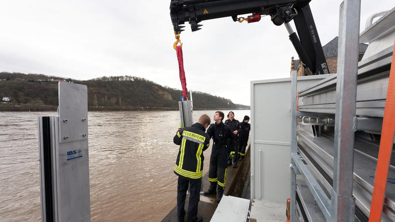 04.02.2020, Rheinland-Pfalz, Koblenz: Feuerwehrleute bauen am Rheinufer des Stadtteils Neuendorf eine mobile Hochwasserschutzmauer auf. Ihre erfolgreiche Bewährungsprobe hatte die in den vergangenen Jahren fertiggestellte mobile Mauer beim Hochwasser