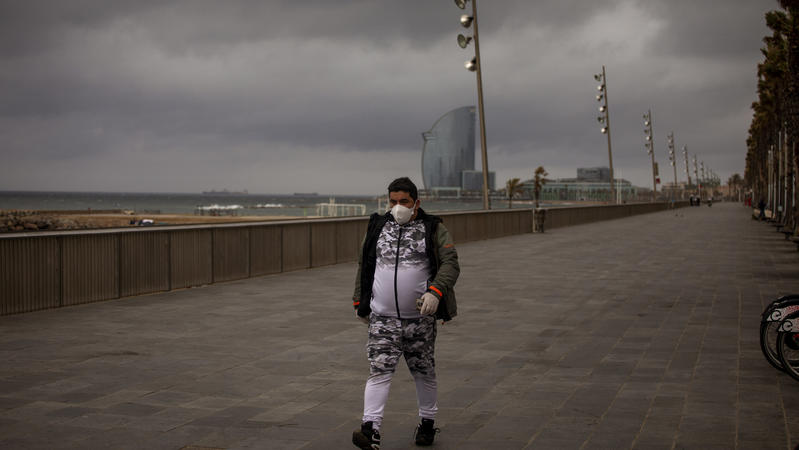 16.03.2020, Spanien, Barcelona: Ein Mann mit Mundschutz geht auf eine leere Promenade in Barcelona. Zur wirksameren Bekämpfung des Coronavirus hat Spanien einen zweiwöchigen sogenannten Alarmzustand verhängt, der auf die Einschränkung der Bewegungsfr
