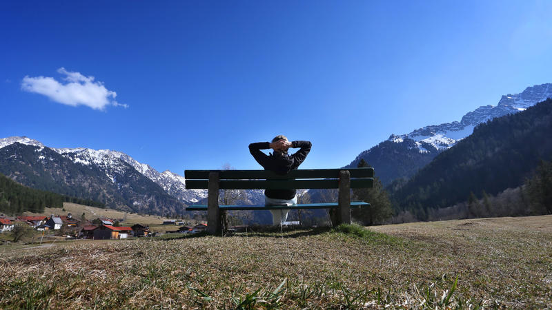 dpatopbilder - 18.03.2020, Bayern, Bad Hindelang: Eine Wanderin genießt auf einer Bank im Hintersteiner Tal den Sonnenschein und die Aussicht auf das Panorama der Berge. Foto: Karl-Josef Hildenbrand/dpa +++ dpa-Bildfunk +++