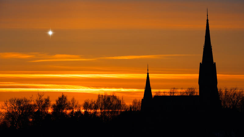 Planet Venus in twilight sky. Sunset clouds behind church towers and treetop silhouettes.