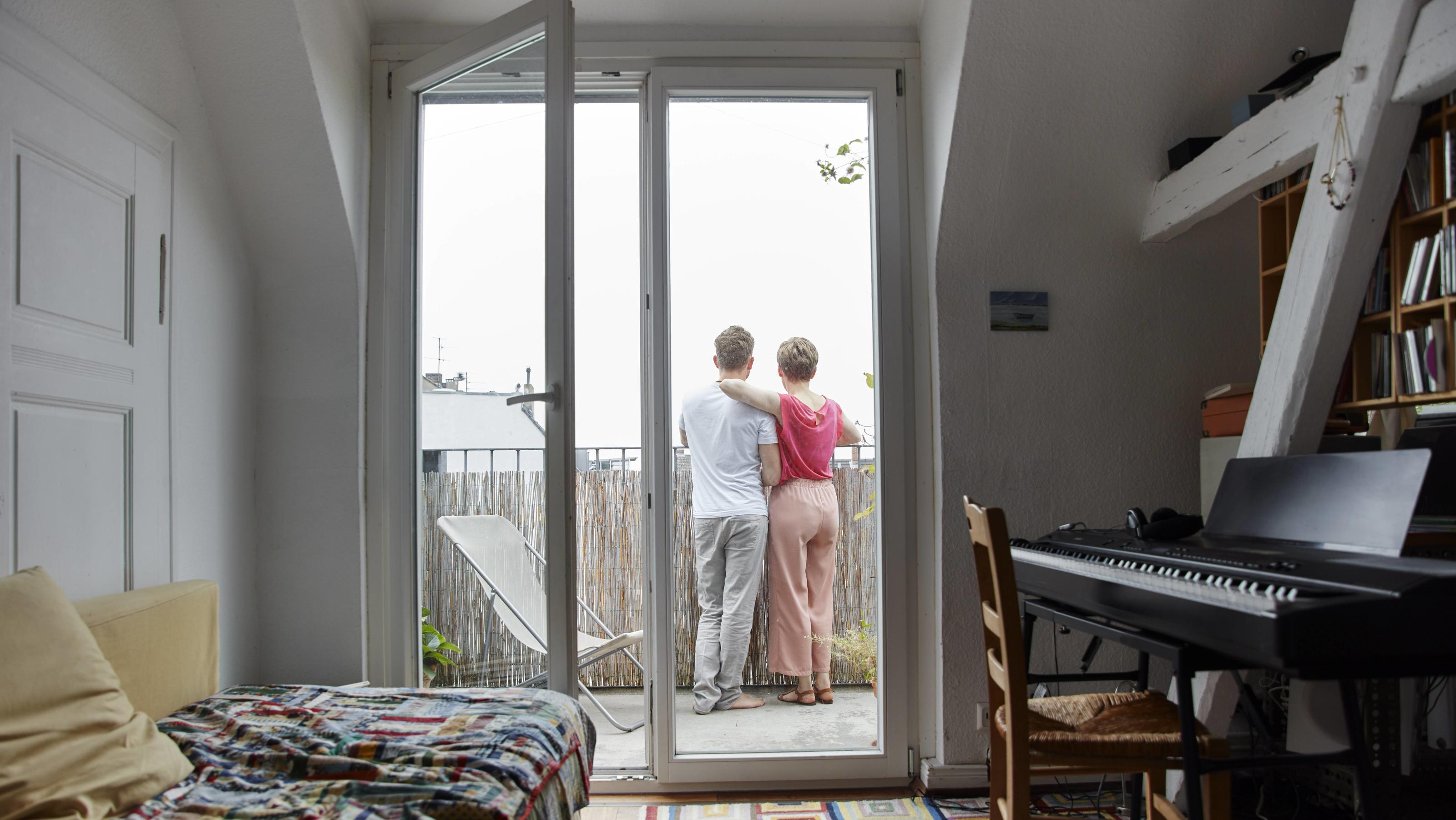 Rear view of couple standing on balcony at home model released Symbolfoto property released PUBLICATIONxINxGERxSUIxAUTxHUNxONLY RHF02300  