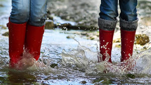 Children wearing rain boots jumping into a mountain river. Close up
