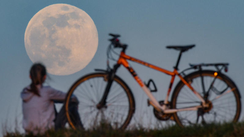 07.04.2020, Brandenburg, Sieversdorf: Der Mond geht als sogenannter Supermond auf, während auf einem Hügel ein Mädchen neben ihrem Fahrrad sitzt und das Schauspiel bewundert. Der Mond erreicht in der Nacht vom 07. auf den 08. April als Vollmond sein