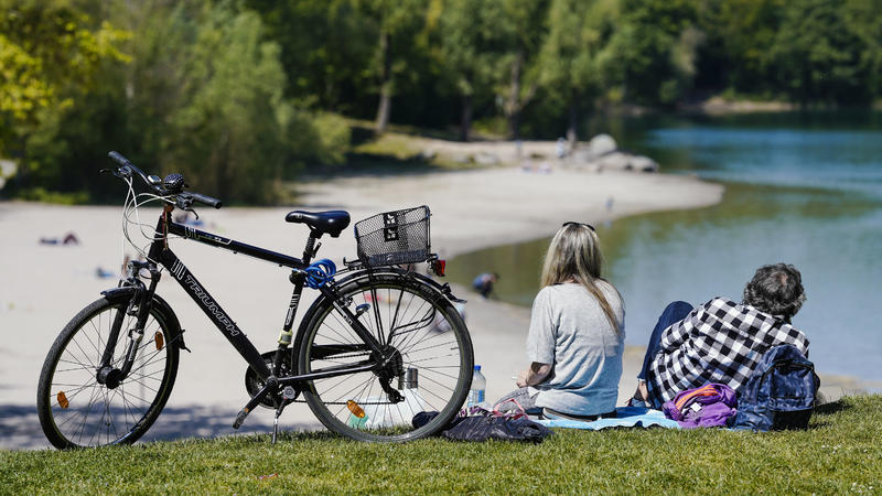 25.04.2020, Baden-Württemberg, Mannheim: Ein Mann und eine Frau sitzen neben einem Fahrrad auf einer grünen Wiese und schauen in Richtung eines Badesees. Foto: Uwe Anspach/dpa +++ dpa-Bildfunk +++