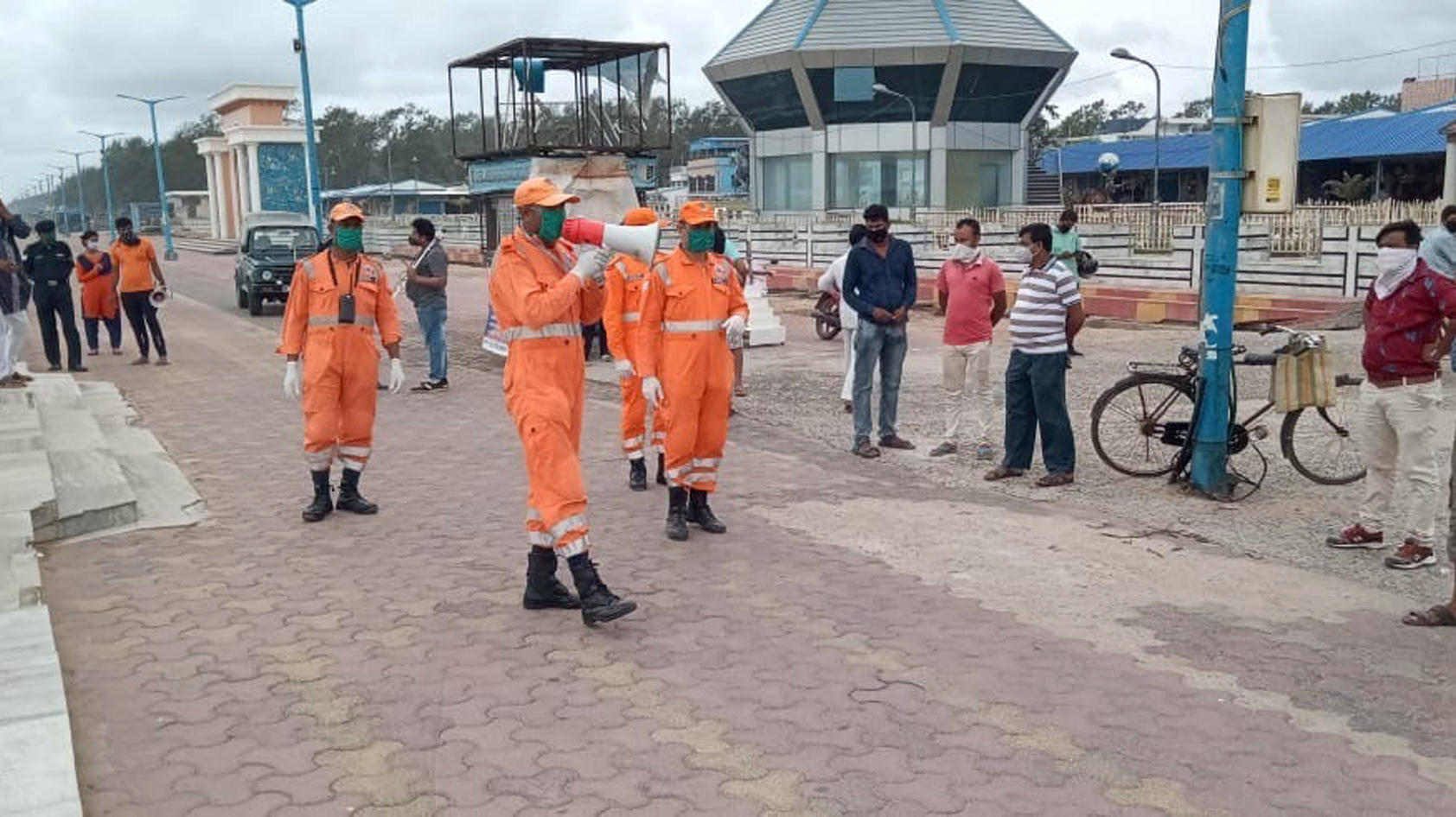 HANDOUT - 19.05.2020, Indien, South 24 Parganas: Mitarbeiter des Katastrophenschutzes stehen an einer Promenade im Golf von Bengalen und sprechen durch ein Megafon mit den Anwohnern. Vor dem Eintreffen eines großen Wirbelsturms in Indien und Banglade