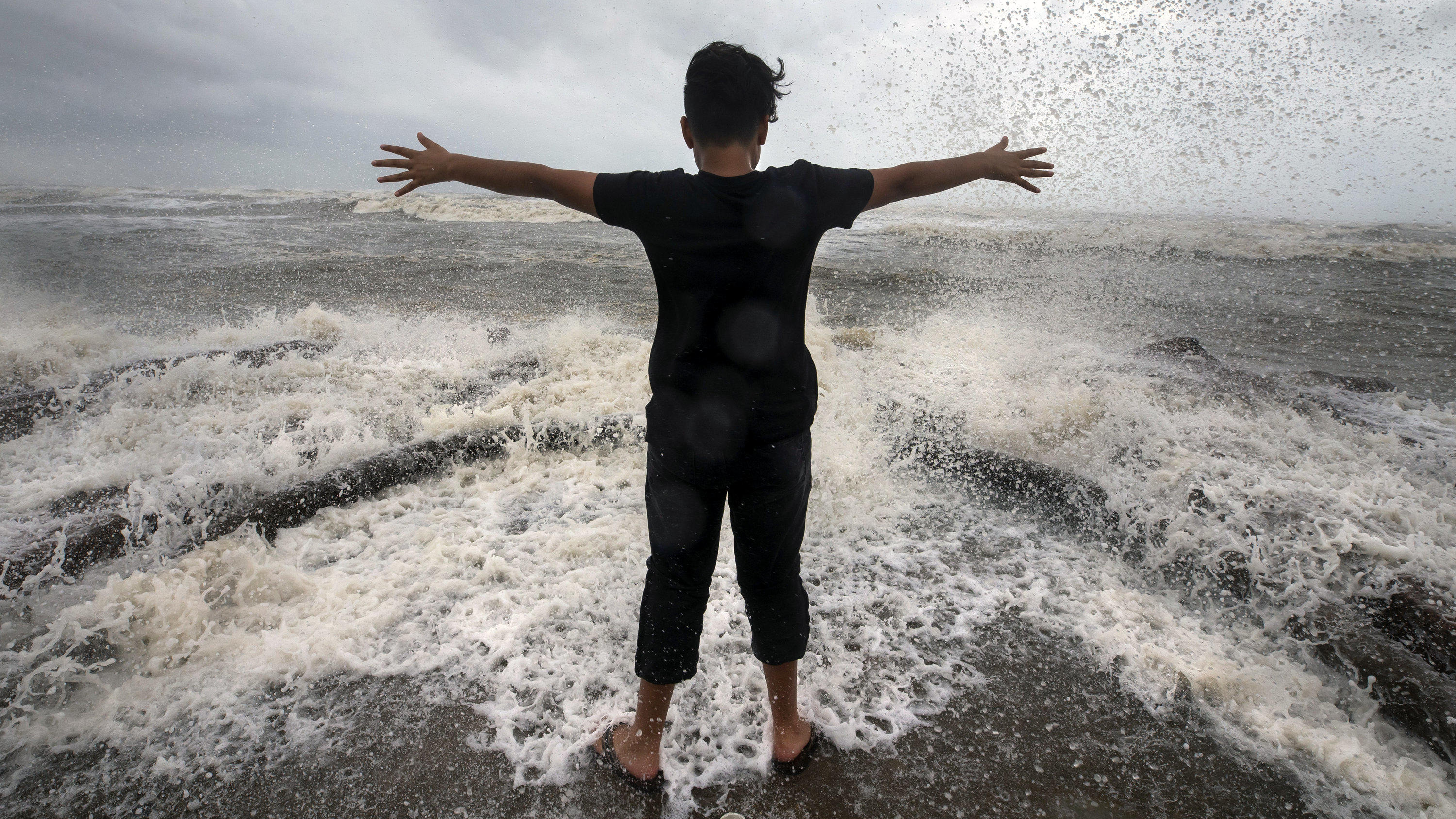 dpatopbilder - 25.07.2020, USA, Galveston: Sahid Ramirez streckt seine Arme zum Wasser aus, während eine Welle vor ihm bricht. Der erste Hurrikan der diesjährigen Saison über dem Atlantik ist im US-Bundesstaats Texas auf Land gestoßen. Foto: Stuart Villanueva/The Galveston County Daily News/AP/dpa +++ dpa-Bildfunk +++