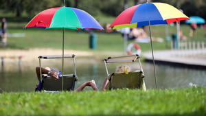 13.09.2020, Baden-Württemberg, Ertingen: Ein Mann und eine Frau liegen unter Sonnenschirmen in Liegestühlen an einem Badesee und halten sich an der Hand. Foto: Thomas Warnack/dpa +++ dpa-Bildfunk +++