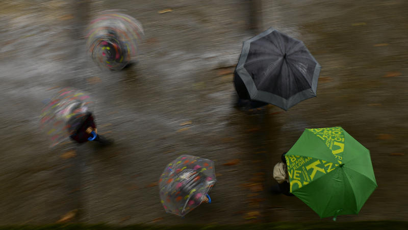 03.10.2020, Spanien, Pamplona: Fußgänger halten Abstand, während sie sich an einem Herbsttag unter Regenschirmen vor dem Regen schützen. Foto: Alvaro Barrientos/AP/dpa +++ dpa-Bildfunk +++
