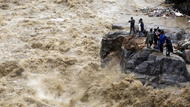 Nepal, Kathmandu: Nepalesen stehen auf einem Felsen am Ufer des überfluteten Flusses Bagmati und fotografieren die Strömung. 
