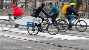 01.12.2020, Bayern, München: Radler, darunter einer mit Surfbrett im Gepäck, fahren über eine verschneite Straße in der Innenstadt. Foto: Peter Kneffel/dpa +++ dpa-Bildfunk +++