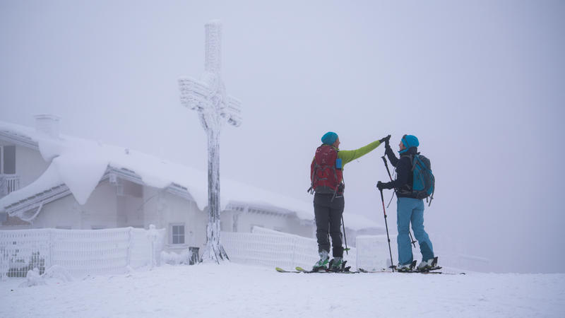 Zwei Skiwanderinnen gratulieren sich zum Erreichen des Gipfelkreuzes auf dem Großen Feldberg im Taunus.