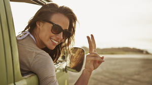 An attractive young woman leaning out the window of a van during a road trip stop
