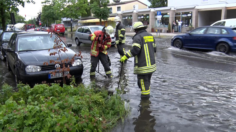 22.06.2021, Bayern, Ottobrunn: Mitarbeiter der Feuerwehr legen nach einem Unwetter Gullys in einer überschwemmten Straße frei, damit das Wasser ablaufen kann. Foto: B & S/dpa-Zentralbild/dpa +++ dpa-Bildfunk +++