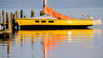 24.06.2021, Niedersachsen, Bad Zwischenahn: Ein gelbes Segelboot liegt in der abendlichen Sonne an einem Steg im Zwischenahner Meer im ruhigen Wasser. Foto: Hauke-Christian Dittrich/dpa +++ dpa-Bildfunk +++
