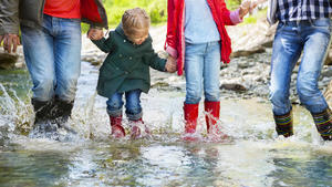 Happy family with two children wearing rain boots jumping into a mountain river