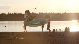 02.07.2021, Finnland, Helsinki: Badegäste tragen ein Schwimmreifen in Form eines Einhorns über den Strand während die Sonne untergeht. Foto: Roni Rekomaa/Lehtikuva/dpa +++ dpa-Bildfunk +++