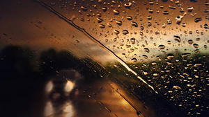 Taillights of cars blurred by rain on windshield during a storm on a busy suburban road in spring. Shallow depth of field, for themes of weather, vision, safety