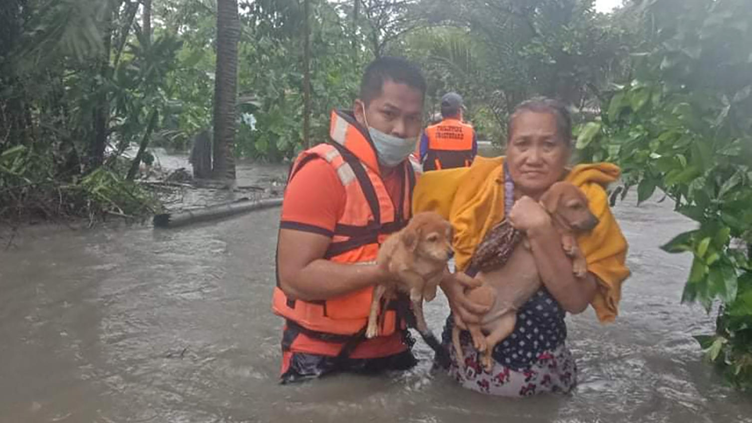 HANDOUT - 09.09.2021, Philippinen, Naic: Ein Mann hilft einer Frau und ihren Hundewelpen durch das Hochwasser, das durch den Taifun «Conson» verursacht wurde. Der Taifun «Conson» hat im Osten der Philippinen zu Stromausfällen in mehreren Provinzen ge