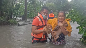 HANDOUT - 09.09.2021, Philippinen, Naic: Ein Mann hilft einer Frau und ihren Hundewelpen durch das Hochwasser, das durch den Taifun «Conson» verursacht wurde. Der Taifun «Conson» hat im Osten der Philippinen zu Stromausfällen in mehreren Provinzen geführt und eine große Suchaktion ausgelöst. Das Wetteramt stufte ihn später zu einem tropischen Sturm herab. Foto: -/Philippines Coast Guard/AP/dpa - ACHTUNG: Nur zur redaktionellen Verwendung und nur mit vollständiger Nennung des vorstehenden Credits +++ dpa-Bildfunk +++