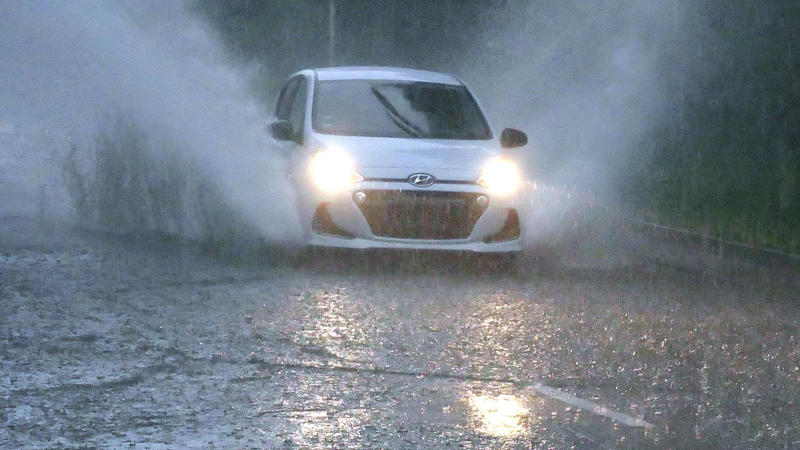 Ein Auto fährt über eine überflutete Straße.