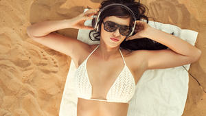 Beautiful girl at the beach on white towel listening music 