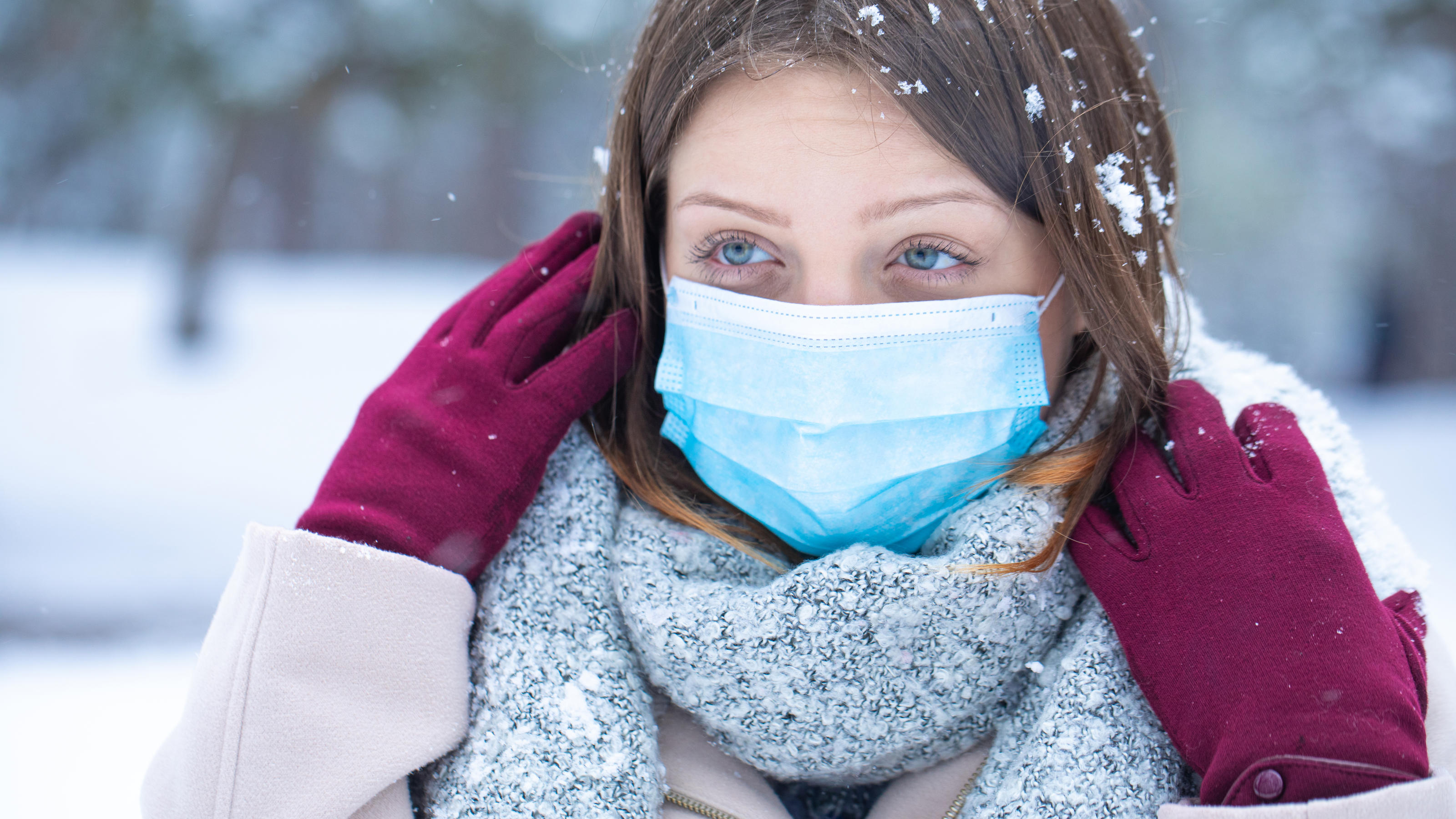 Eine junge Frau trägt winterfeste Kleidung im Schnee und eine Mund-Nasenschutz-Maske, um sich vor dem Coronavirus zu schützen.