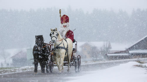 Ein als Nikolaus verkleideter Mann ist mit einer von zwei Ponys gezogenen Kutsche im Schneetreiben unterwegs.