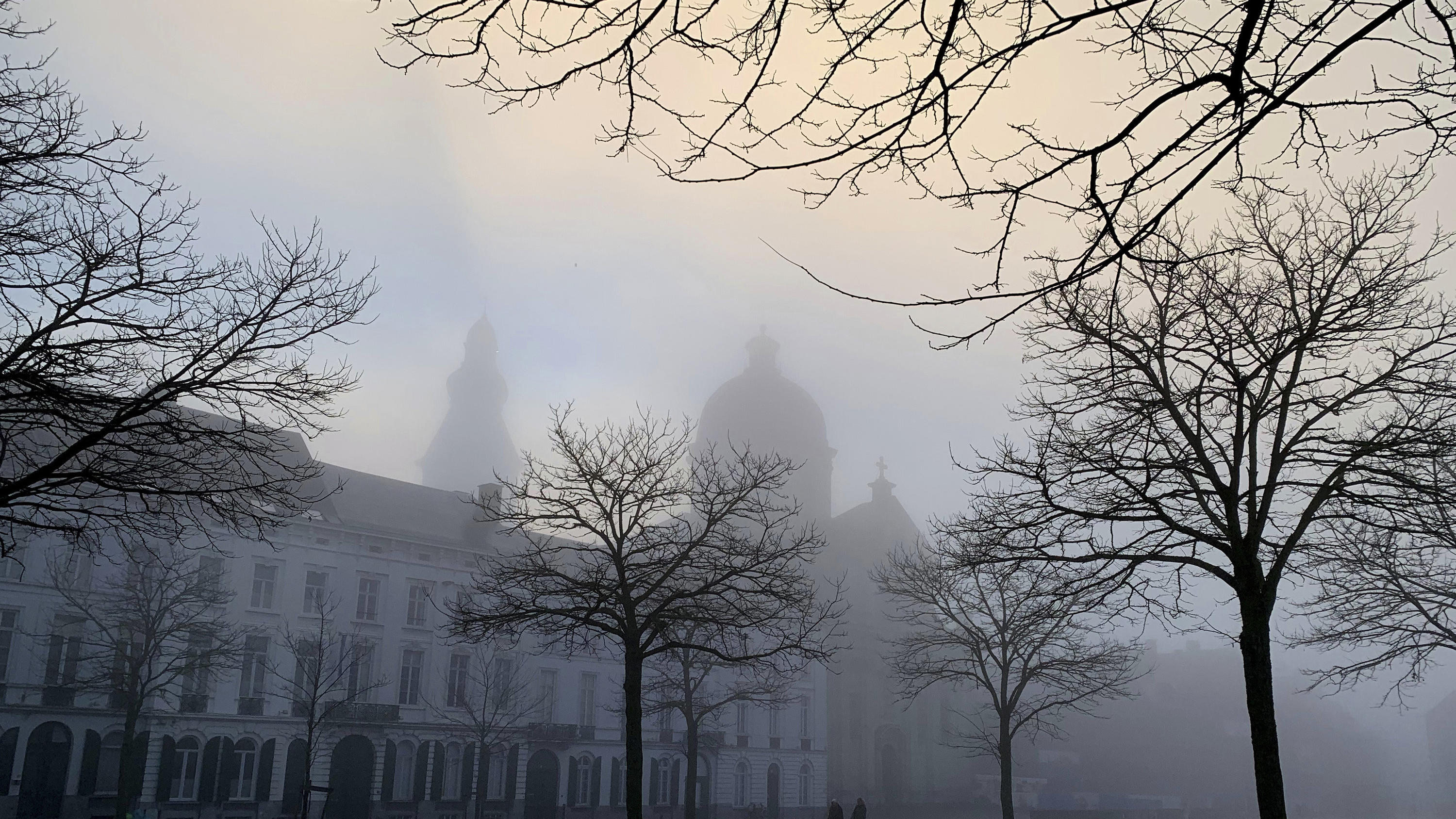 14.01.2022, Belgien, Ghent: Zwei Personen spazieren in einem Innenhof, während sich Nebel vor der Abtei Saint-Pierre bildet. Foto: Virginia Mayo/AP/dpa +++ dpa-Bildfunk +++