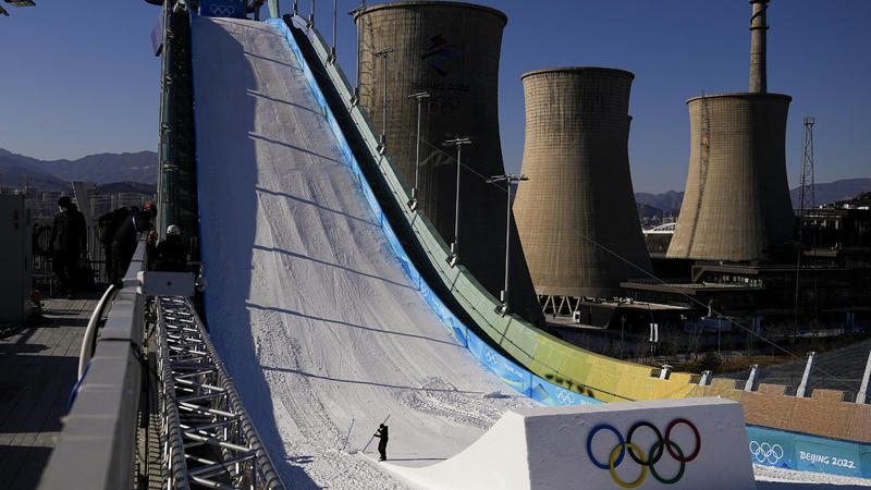 Ein Arbeiter formt den Kicker auf dem Big Air Shougang im Vorfeld der Olympischen Winterspiele 2022. Im Hintergrund sind die alten Kühltürme eines Stahlwerks im ehemaligen Industriegebiet der Stadt zu sehen.