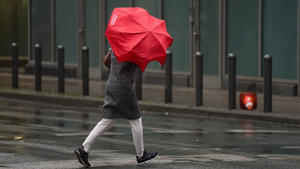 06.02.2022, Hessen, Frankfurt/Main: Eine Frau überquert bei stürmischem Wind und Regen eine Straße in der Frankfurter Innenstadt. Foto: Frank Rumpenhorst/dpa +++ dpa-Bildfunk +++