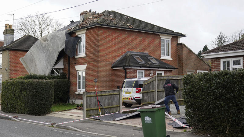 A man cleans up a driveway after a flat roof from a nearby block of flats was blown off and landed on a house in Bitterne, Southampton, England, Saturday Feb. 19, 2022. Crews cleared fallen trees and worked to restore power to about 400,000 people in