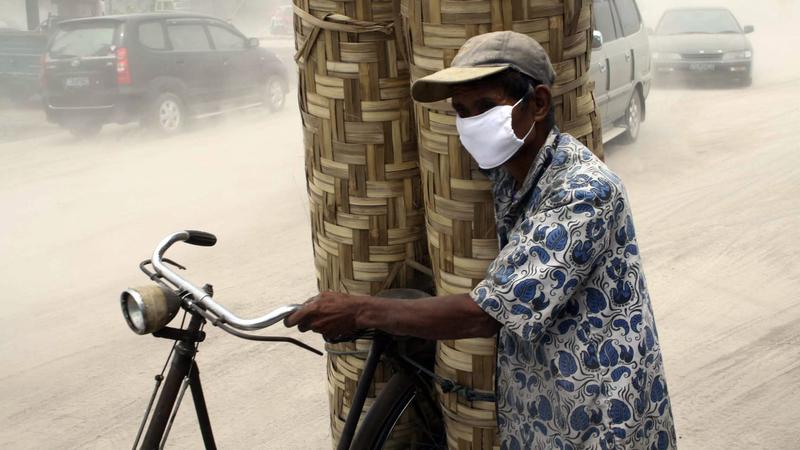 An Indonesian man wears protective mask as he carries woven bamboo walls on his bike on a ash covered motorway after mount Merapi erupted in Yogyakarta, Indonesia, 30 October 2010. Indonesia's Mount Merapi volcano with 2,968 meters high in Central Ja