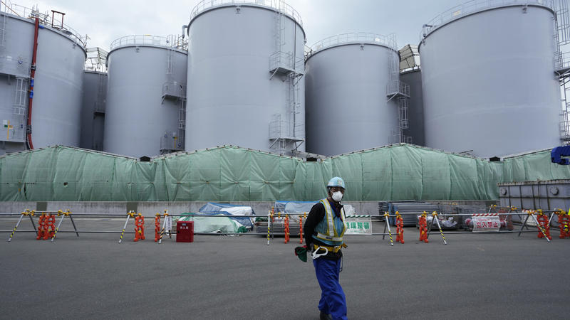 A worker helps direct a truck driver as he stands near tanks, background, that will be used to store treated radioactive water after it was used to cool down melted fuel at the Fukushima Daiichi nuclear power plant, run by Tokyo Electric Power Compan