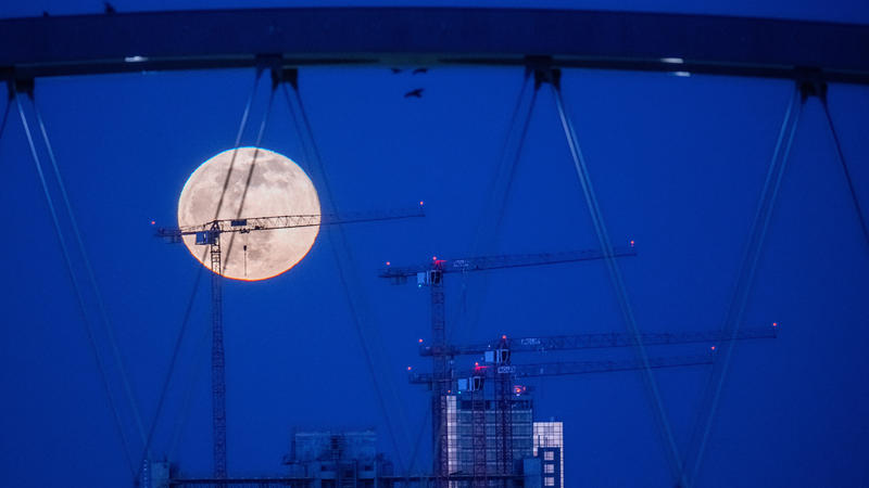 18.03.2022, Hessen, Frankfurt/Main: Der Mond steht über Offenbach am Main. Dabei sind im Vordergrund Baukräne und der Rohbau eines Häuserkomplexes zu sehen. Foto: Boris Roessler/dpa +++ dpa-Bildfunk +++