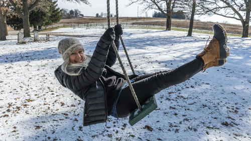 Smiling woman on swing in snow, Laechelnde Frau auf Schwingen im Schnee || Modellfreigabe vorhanden