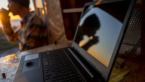 Laptop on desk in camper van with sunset reflected in screen, working remotely.
