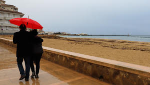 25.12.2020, Spanien, Palma: Ein Paar spaziert mit einem Regenschirm am Strand von Palma entlang. Kälte und Regen kennzeichnen die Wettervorhersage auf Mallorca für die nächsten Tage. Foto: Clara Margais/dpa +++ dpa-Bildfunk +++