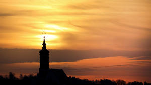 13.04.2022, Baden-Württemberg, Munderkingen: Hinter der Pfarrkirche St. Dionysius geht am Morgen die Sonne auf und beleuchtet dabei auch den Saharastaub, der in der Luft liegt. Foto: Thomas Warnack/dpa +++ dpa-Bildfunk +++