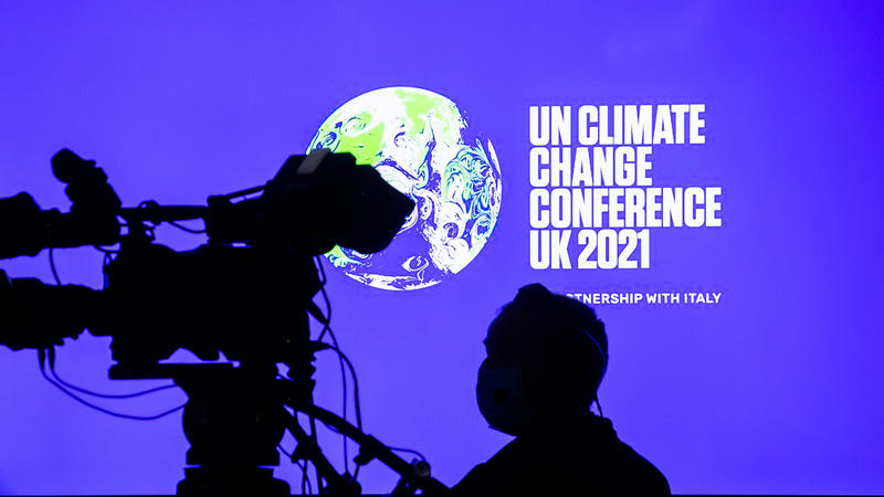 ARCHIV - 09.11.2021, Großbritannien, Glasgow: Ein Kameramann steht bei der UN-Klimakonferenz COP26 in Glasgow vor einem Bildschirm mit dem Weltklimakonferenz-Logo. (zu dpa: «WMO: 1,5-Grad-Schwelle könnte bis 2026 erstmals überschritten werden») Foto: