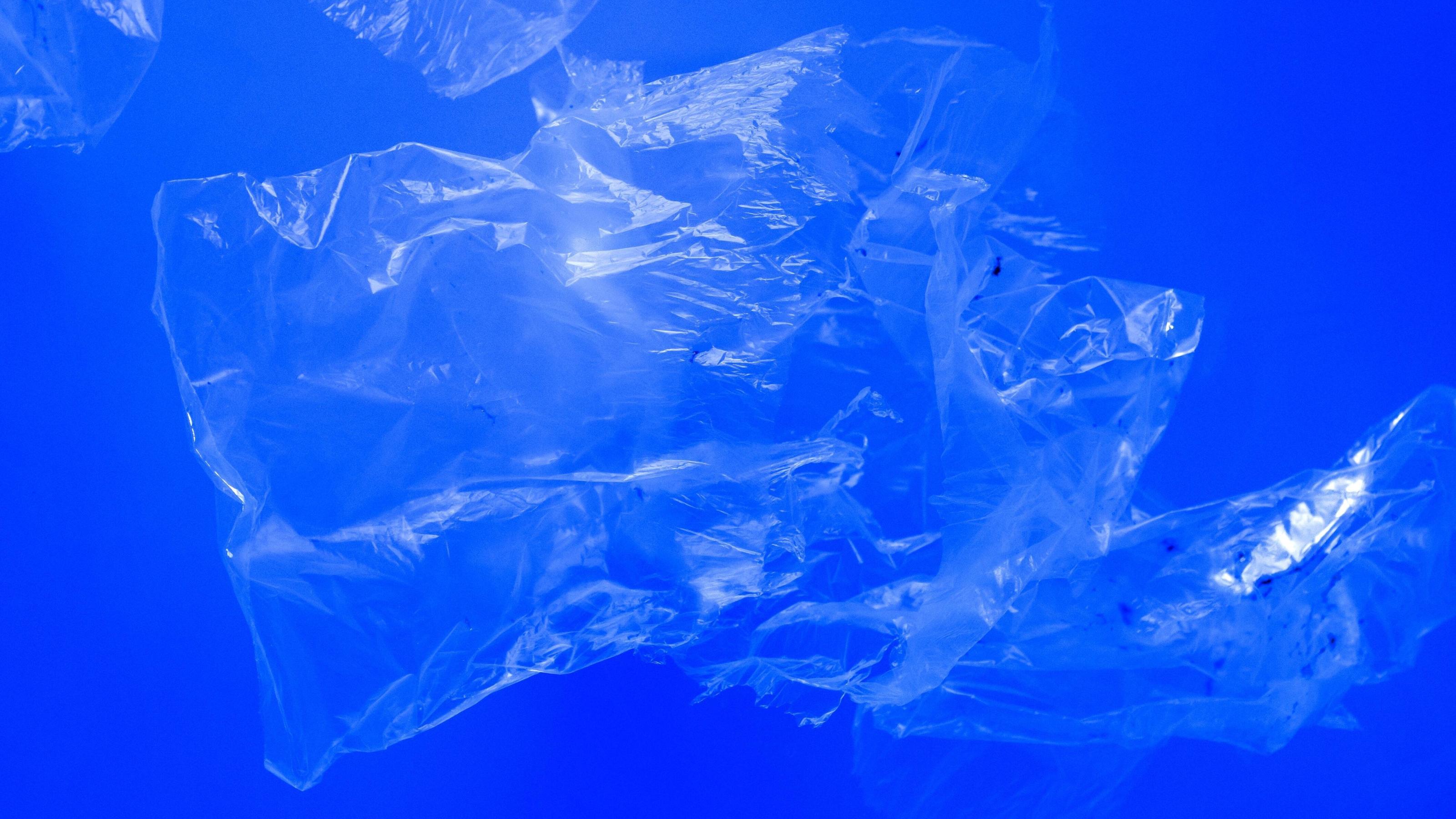 Transparent plastic bags floating underwater in blue ocean sea water, pollution by non-biodegradable plastic waste, hazard for marine wildlife 333DYKCS