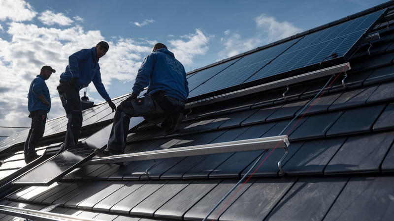 Mitarbeiter der Firma Sontec GmbH montieren Photovoltaikmodule auf dem Dach eines Wohnhauses.