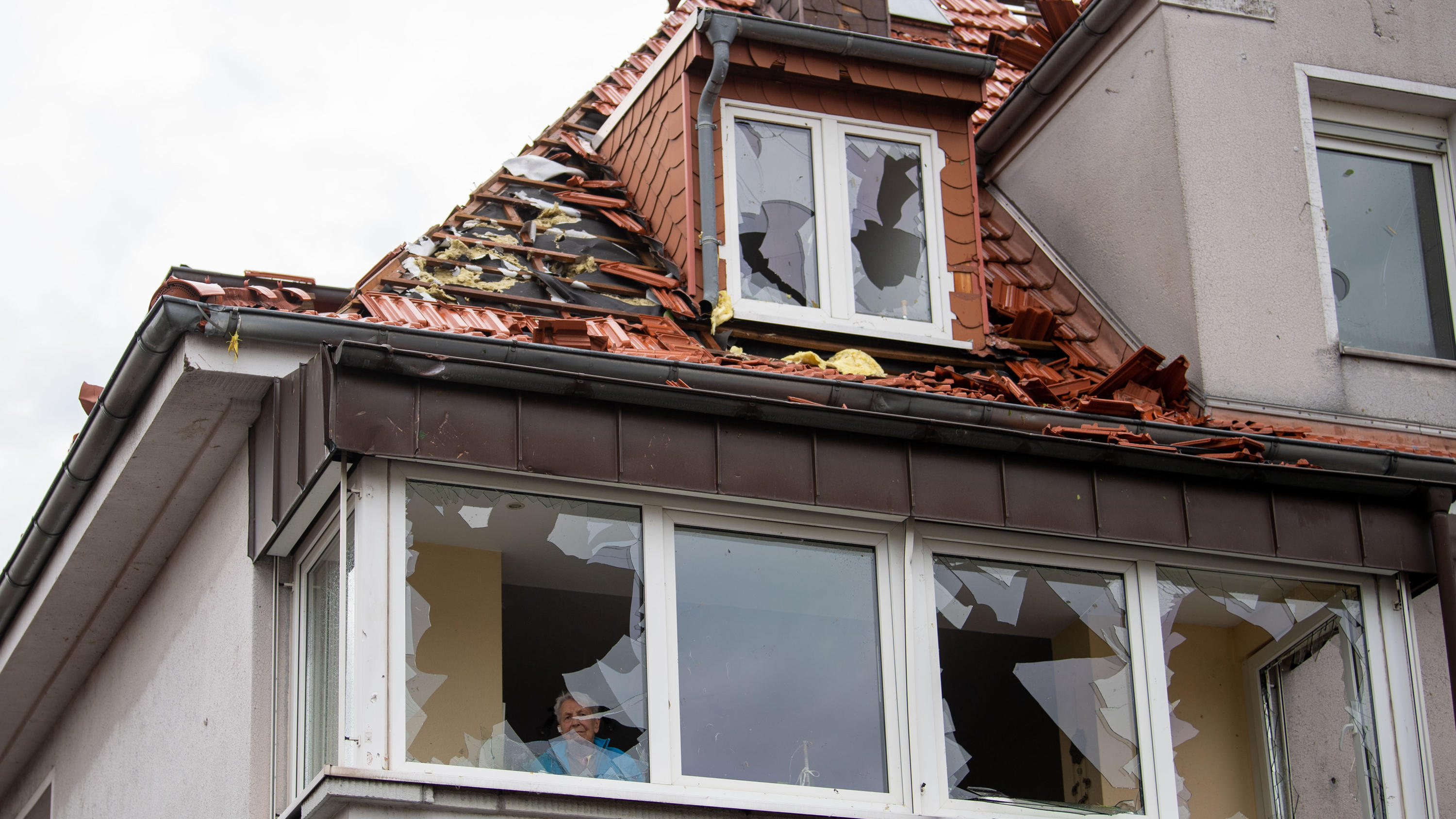 20.05.2022, Nordrhein-Westfalen, Paderborn: Eine Anwohnerin schaut aus einem der zerbrochenen Fenster ihrer Wohnung. Ein Unwetter hat auch in Paderborn große Schäden angerichtet. Foto: Lino Mirgeler/dpa +++ dpa-Bildfunk +++