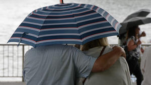 Besucher der Rheinpromenade vor der Kölner Altstadt schützen sich mit einem Schirm vor einem Regenschauer.
