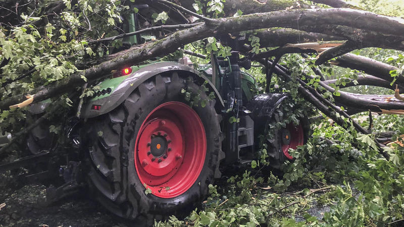 Ein dicker Baum ist auf einen Traktor gestürzt. Eine Gewitterfront hat am Donnerstagabend im Rheinland Schäden verursacht. Der Deutsche Wetterdienst hatte vor der Gewitterfront mit Starkregen gewarnt.