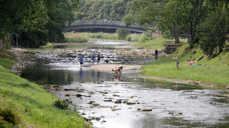 Menschen genießen am 05.07.2015 am grünen Ufer der Ahr in Bad Neuenahr-Ahrweiler (Rheinland-Pfalz) das sommerliche Wetter und kühlen sich im Wasser ab.