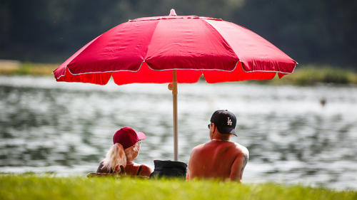 19.06.2022, Baden-Württemberg, Ertingen: Ein Mann und eine Frau liegen an einem Badesee unter einem Sonnenschirm im Schatten. Für den Tag sind laut Meteorologen wieder Temperaturen um 35 Grad Celsius vorhergesagt. Foto: Thomas Warnack/dpa +++ dpa-Bildfunk +++